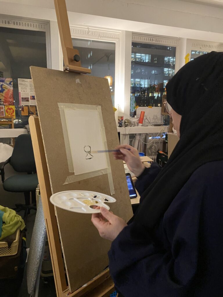 Mother painting with oil paints at Sketchbook Club, sharing her skills with other participants.